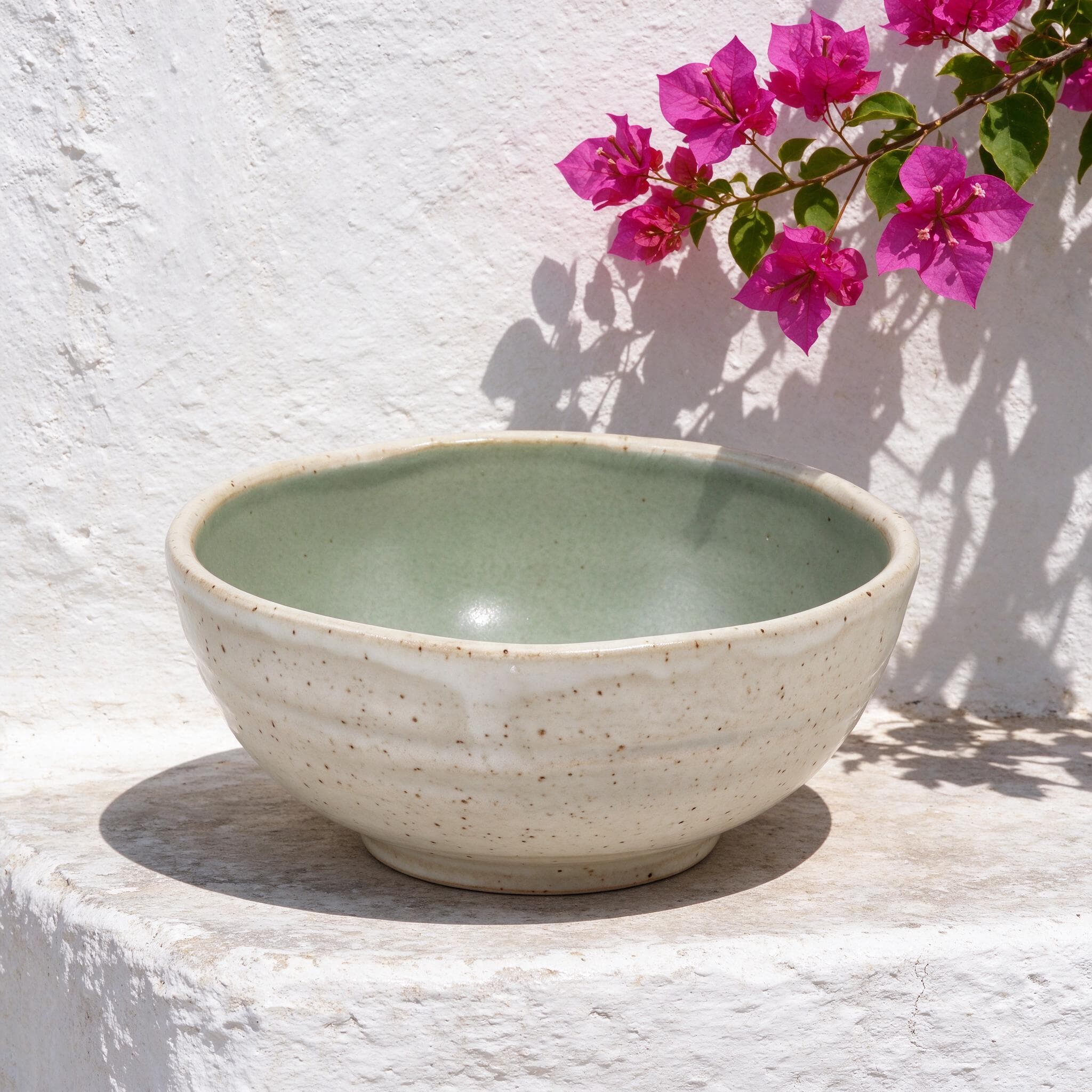 Speckled ceramic bowl with a green interior on a sunlit whitewashed ledge beneath magenta bougainvillea